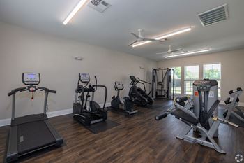 a gym with cardio machines and other exercise equipment on a wooden floor at Beau Chene Lake Charles Apartments in Lake Charles, LA 70605